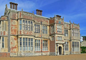A picture of Felbrigg Hall, which is built from red brick & flint. The hall has large windows and nine visible chimneys.