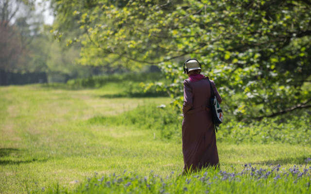 Photo from NNF16 show Walk With Me, a woman dressed in a long purple coat, wearing a pair of headphones and walking through a field.