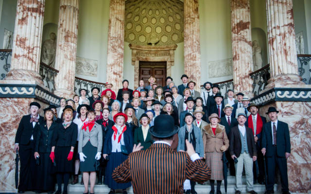 Photo from NNF14 show Souvenir, a group of approx forty choir members dressed in 1920s attire stand on a grand staircase.