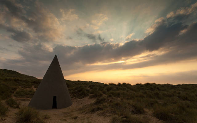 Photo from NNF12 show Walking, a large cone with a small cut out door sits on a sand dune.