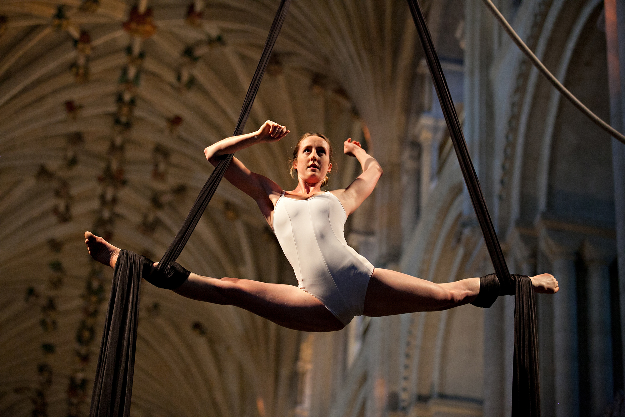 Photo from NNF12 show How Like An Angel, a woman performs the splits in mid-air while hanging from two pieces of silk.