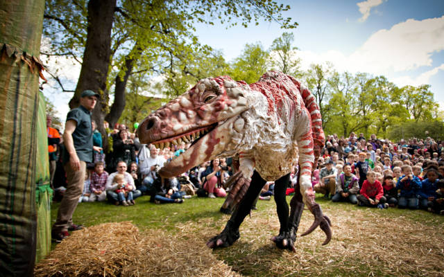 Photo from NNF12 show Dinosaur Petting Zoo, a large T-rex puppet faces the camera, behind it is a large crowd of children.