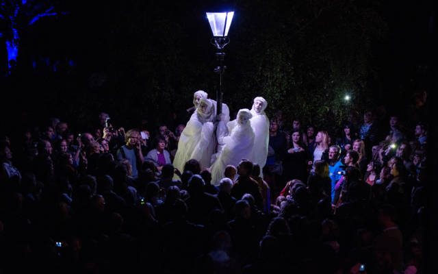 Photo from NNF13 show Reve dHerbert, four men standing on tall stilts dressed all in white, hold onto an old style street lamp. They are surrounded by a large crowd.