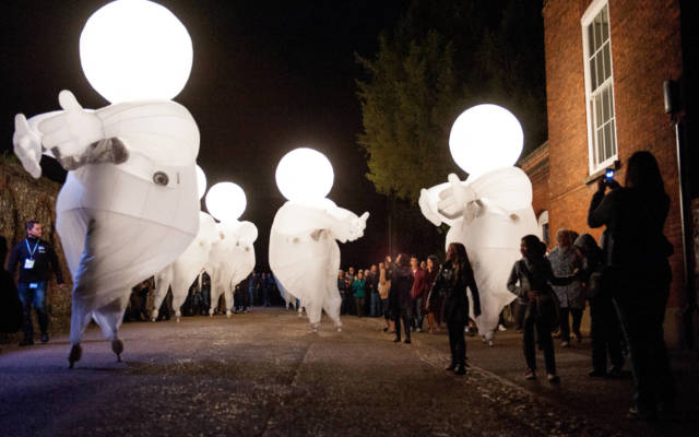 Photo from NNF13 show Reve dHerbert, seven large white glowing figures walk down the street, a large crowd is following them.