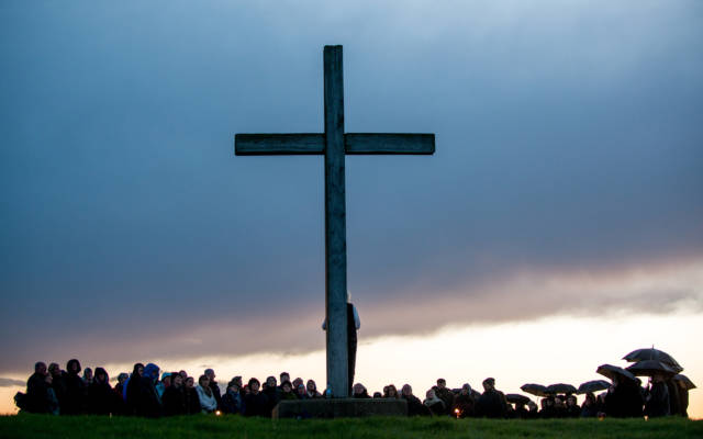 Photo from NNF13 show Ideas of Flight, a large audience watch a man who is standing in front of a huge wooden crucifix.