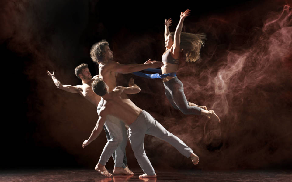 Publicity photo for NNF18 show Shift, three members of Barley Methodical Troupe stand on the left, preparing to catch a fourth performer who is jumping in from the right of the frame.