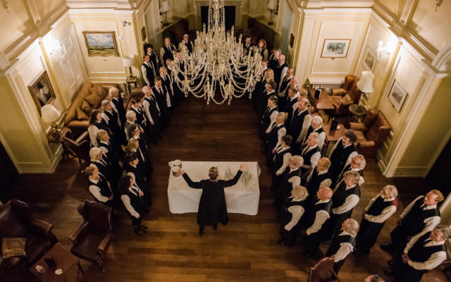 Photo from NNF17 show The Arms of Sleep, taken from above. The Voice Project Choir stand in a semi-circle with a table in between them.