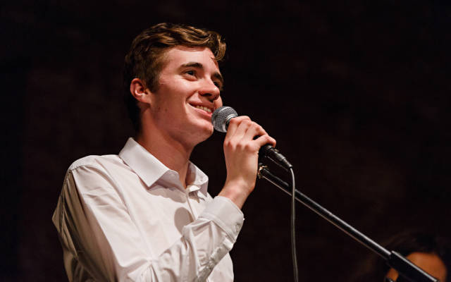 Photo from NNF16 show Wild Life, a man is looking out of frame, smiling and holding a microphone up to his mouth.