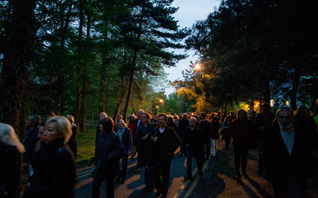 A large crowd walking through a wooded area at dusk.