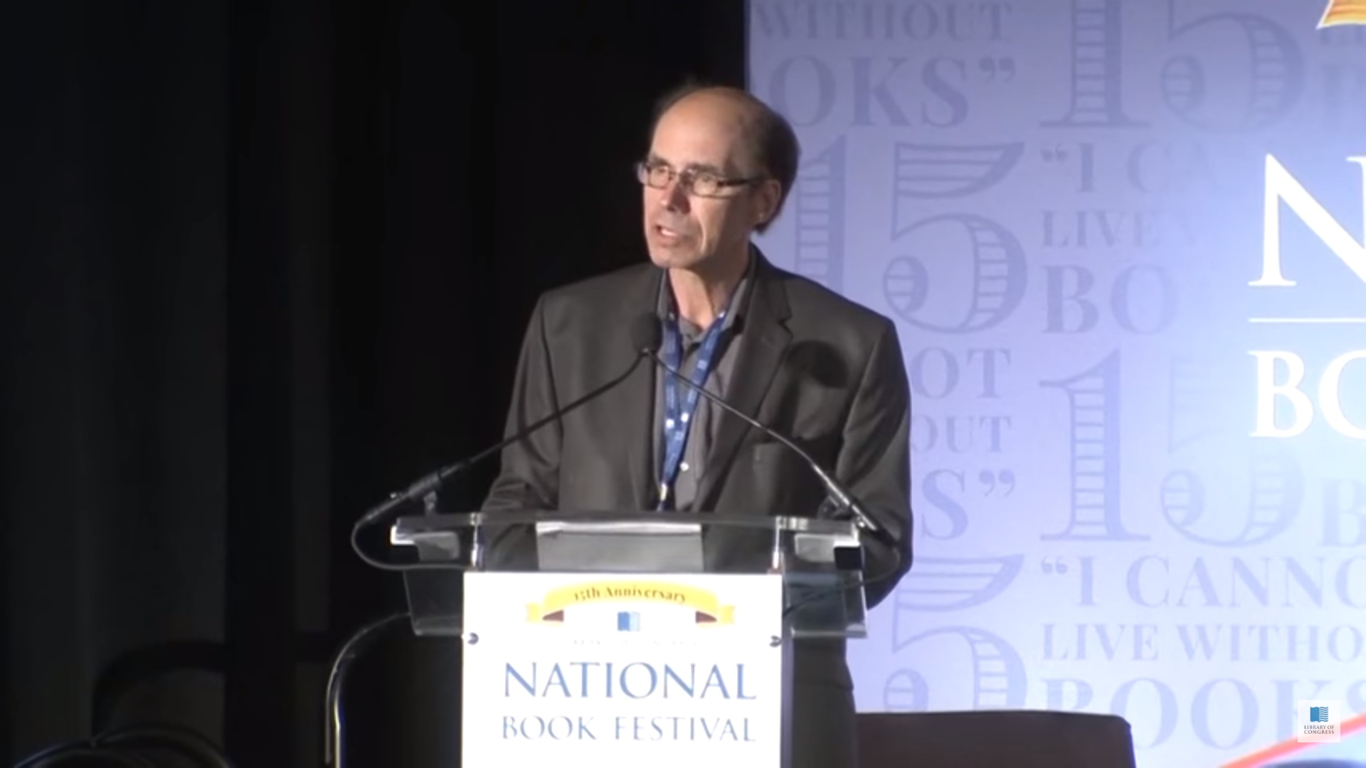 Jeffery Deaver stands behind a podium, talking at an event.
