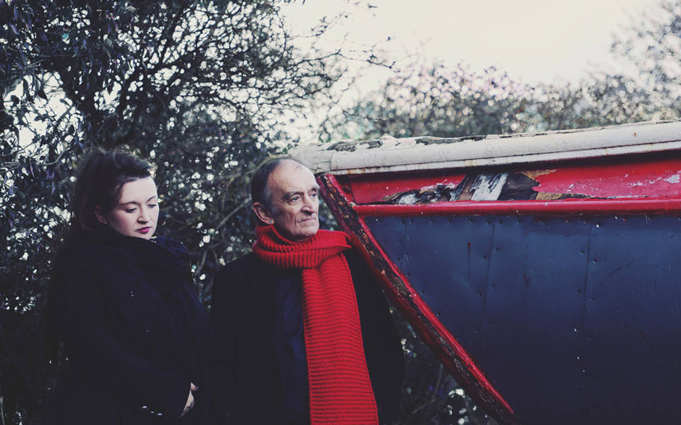 Eliza and Martin Carthy stand at the edge of a boat wrapped up in coats and scarves