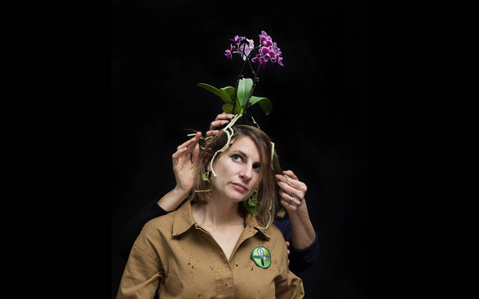 Photo: a woman with an orchid on her head, seemingly disembodied hands adjusting the flower