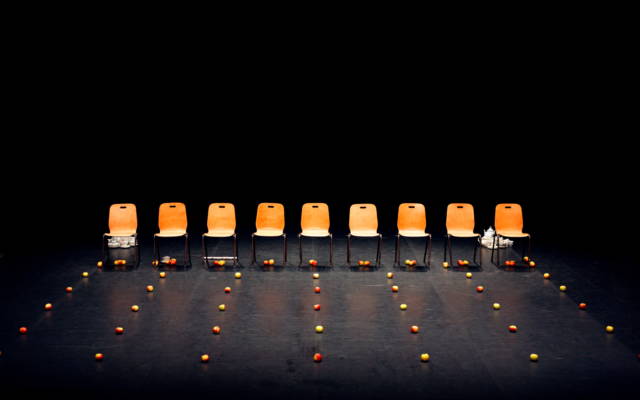 A row of empty chairs with rows of apples in front of them