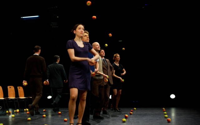 A group of men and women stand in a row juggling apples