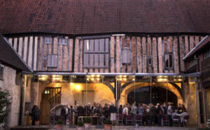 Photo: view of Dragon Hall from the back garden, venue is illuminated inside by soft light, a crowd of people gathering