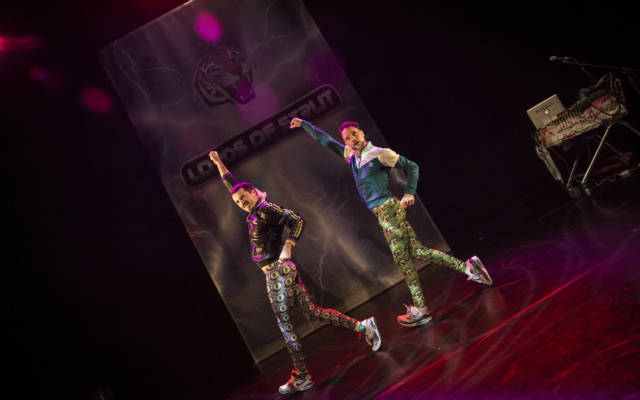 Photo: Two men wearing bright lycra trousers and sports jacks dance in sync