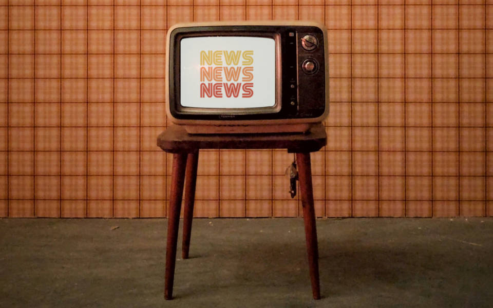 Photo: an old TV on a stool in front of an orange background. News News News logo shown on the TV. 70s style.