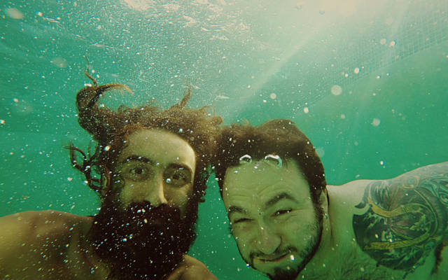 Photo: two men underwater, surrounded by bubbles, smiling to the camera