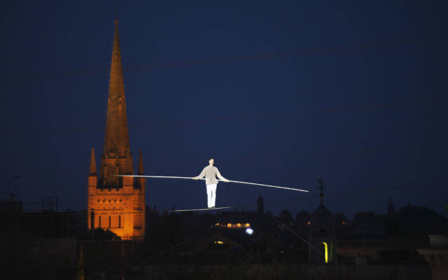 Highwire artist Chris Bullzini walking the highwire, Norwich Cathedral illuminated in the background.