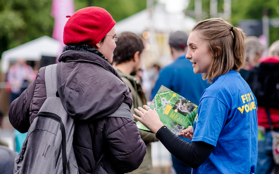 A volunteer at the Festival's Garden Party hands a flyer to a passer-by