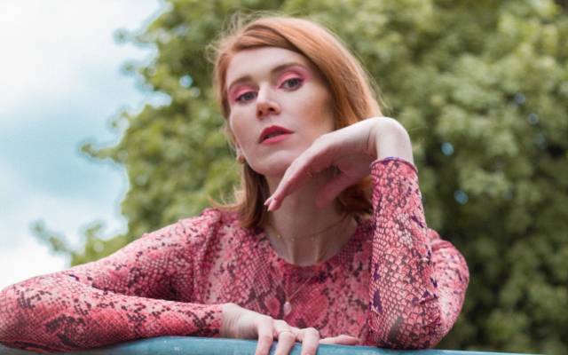 Ellena Woolf rests arm on railings whilst looking at camera