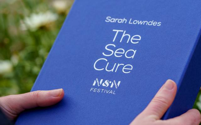 Hands holding a blue box with 'The Sea Cure' in silver text