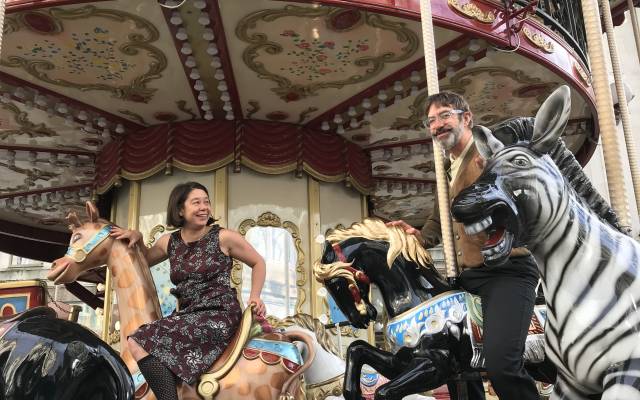 a woman and a man sit on old fashioned carousel and smile at each other