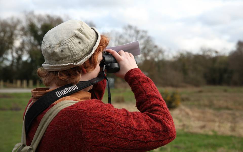 Person looking through binoculars in a nature reserve.