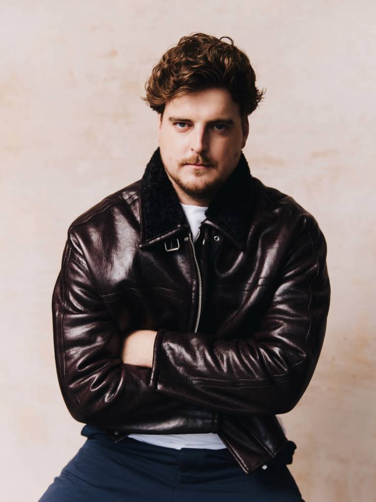 A white man in a leather jacket looks toward the camera.